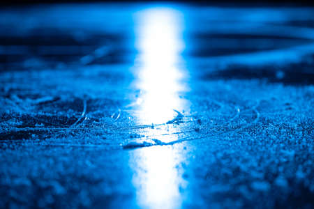 Ice background and texture with scratches from skating and hockey. Ice rink floor, detail of textured ice background with snow and crystals in blue light. Empty ice rink close up.の写真素材