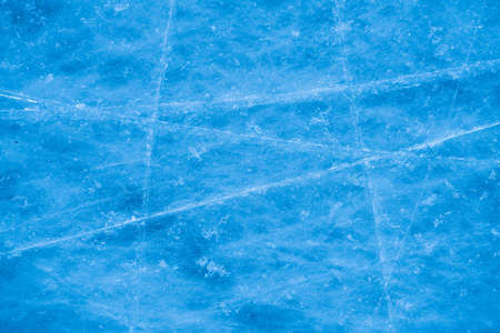 Ice surface in sports arena for figure skating or hockey. Ice background and ice texture is cut with pattern and scratches from skates. Detail of textured ice with snow in blue light. Close up.の写真素材