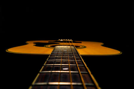 Wooden acoustic guitar with fretboard and strings over black studio background. Stringed plucked...