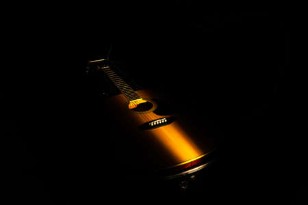 Beam of light illuminates a yellow wooden acoustic guitar. Stringed musical instrument on a black background in the dark. Musical instrument for playing chords and melodies. Guitar in cover close up.の写真素材