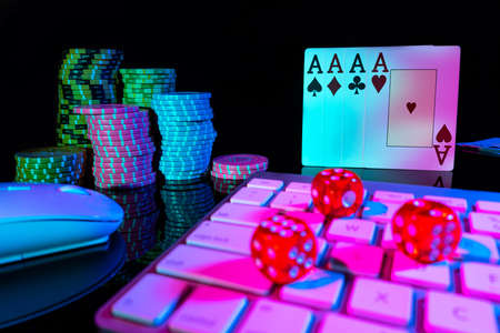 Computer keyboard and quads of four aces, illuminated with pink light on black background. Cards,...