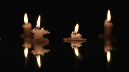 Burning candles on a black background, candlelight reflecting on glossy surface. Stubs of paraffin...