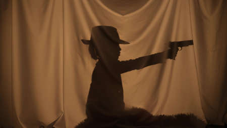 Silhouette of little boy wearing cowboy hat and holding toy gun. Child of primary age have fun,...