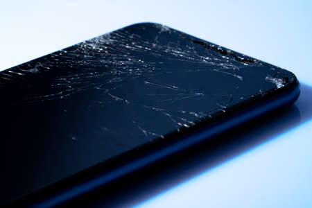 Black crashed smartphone with broken screen on white background. Mobile phone with cracked display glass. Modern phone with cracks on the touchscreen. Destroyed Gadget. Repair concept.の写真素材