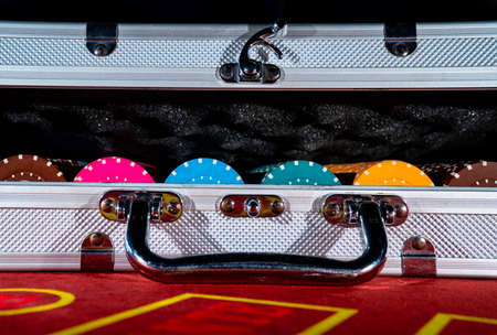 An open suitcase with a set of multicolored casino chips on a red gambling table. Gambling...