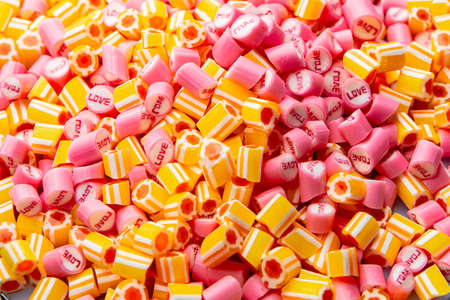 Bunch of pink with inscription Love and yellow striped caramel candies. Mix of colorful sweetmeat...