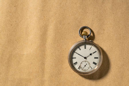 Silver vintage pocket watch with hands and numbers on a round dial. Old retro clock on a beige...