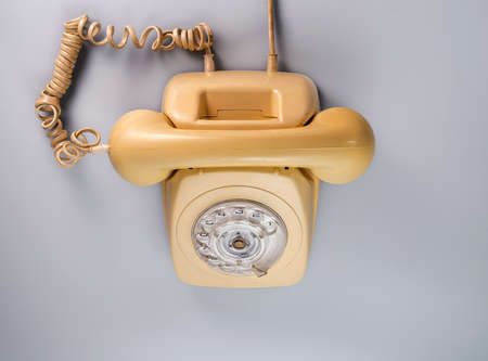 Old yellow antique rotary telephone on blue background. Vintage landline home phone with dial, twisted cable and reciever handset. Communication, telecommunication, conversation apparatus. Top view.の写真素材