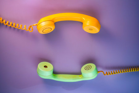 Yellow and green telephone receivers with twisted cords from an old antique rotary phones on purple background. Plastic removed handsets from retro phone with cable. Concept of communication. Top viewの写真素材