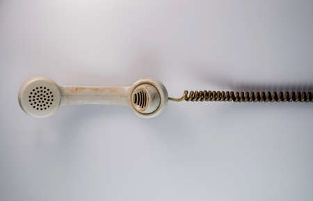 Dirty white remote telephone receiver from an old rotary landline phone with twisted cord on gray background. Plastic vintage handset with telephone cable. Retro home conversation apparatus. Top view.の写真素材