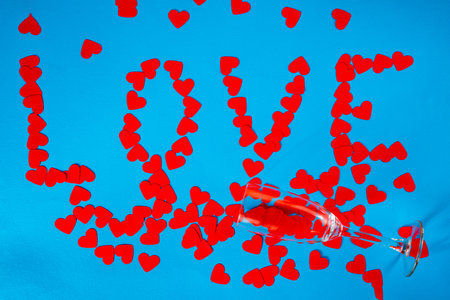 Wineglass and word love from paper red hearts on blue screen background. Top view of heart shaped confetti arranged in a circle around a glass. Screensaver mockup for Valentines day, holiday, party.の写真素材