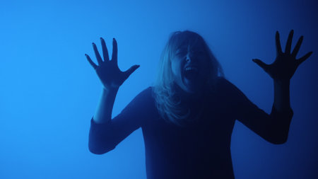 Woman touches glass with palms and and screams in fear and horror. Woman face behind glass conveys...
