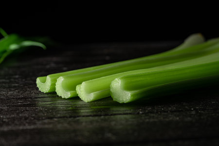 Row of green celery stalks lying on black board on isolated black studio background. Macro shot of...