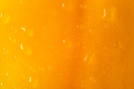 Macro shot of yellow peel of a sweet pepper or tomato with water drops. The texture of the yellow wet surface of a vegetable covered with drops of moisture or dew. Yellow background.の写真素材
