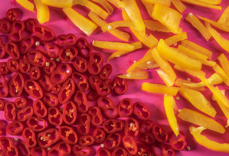 Sliced pieces of yellow sweet pepper and rings red hot chili pepper on a pink background. Top view...