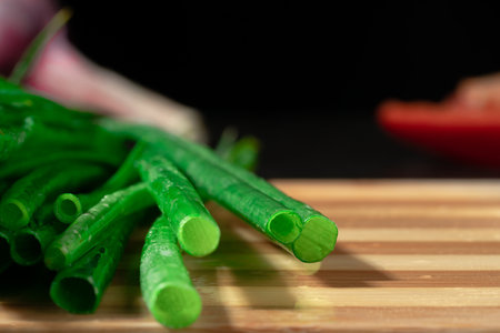Stems of fresh green onions on striped wooden kitchen board. Macro shot of juicy cut stalks of green scallion on black background. Cutaway green shallot or chive stalk. Greenery, seasoning.の写真素材
