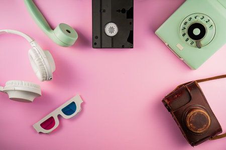 Camera, 3D glasses, videotape. Rotary phone, telephone handset, white headphones, brown leather camera case on pink background with copy space. Retro, vintage, history, nostalgia concept. Top viewの写真素材