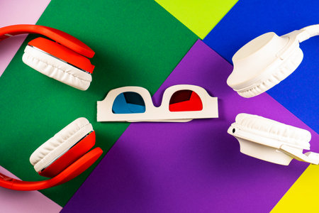Old white paper 3d glasses with blue and red lenses and white red headphones on vintage color background. Retro stereoscopic 3D cardboard glasses. Retro, vintage, history, nostalgia concept. Top view.の写真素材