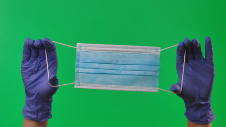 Woman hands in latex blue gloves is showing blue medical protective mask. Doctor arms in protective...