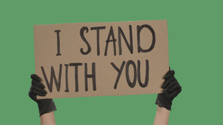 Hands of an unknown person in black gloves raise cardboard poster I STAND WITH YOU. Stop Racism concept, No Racism. Rallies against racism and police brutality. Isolated green screen chroma key.の写真素材