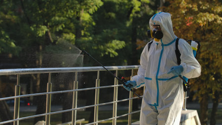 A virologist in a white protective suit and respirator disinfects railings on city streets. Disinfection of objects with antiseptic spray to prevent the spread of the Covid 19 outbreak.の写真素材