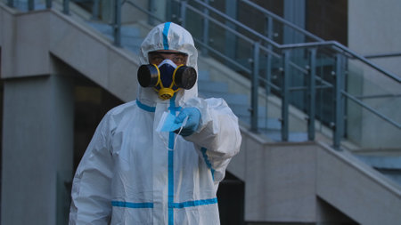 Medical worker or virologist in a white protective suit, goggles and a respirator, showing...