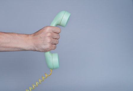 Male hand holding an old blue plastic telephone receiver on gray background. Close up remote handset from a retro rotary home phone in the hands of man. Concept of communication, conversation.の写真素材