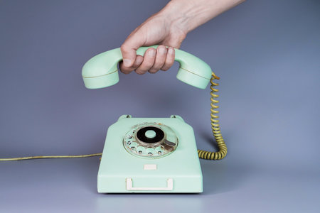 Mans hand laying an old plastic telephone receiver on the levers of a telephone on a gray background. Close up remote handset from a retro rotary home phone in the hands of a man. End of conversation.の写真素材