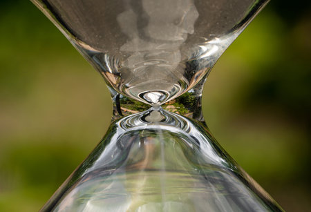 Macro shot of a glass hourglass case against a blurred green nature background. Vessel of...