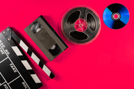 Compact disc, filmstrip bobbin, black plastic video cassette and clapper board on pink background. Old storage media, drives for watching videos or movies or listening to music.の写真素材
