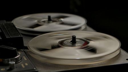 Vintage professional analog reel to reel tape recorder on black studio background. Transparent rotating coils reproduce old music. Analog recorder rewinding tape, torque. Retro tape. Close up.の写真素材