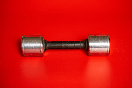 One metal silvery dumbbell lying on red background. Dumbbell for pumping muscles. Sports equipment...
