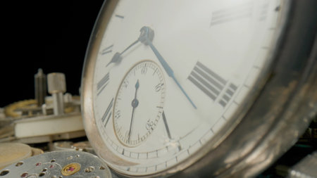 Grey vintage pocket watch dial on pile of clockwork parts. Round old clock among metal gears and...