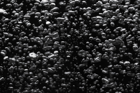 A lot of shiny air bubbles of different sizes underwater on a black isolated background. Close up of light lit oxygen bubbles flow upwards. Aeration or filtration of liquid. Fizzy flow of air bubbles.の写真素材