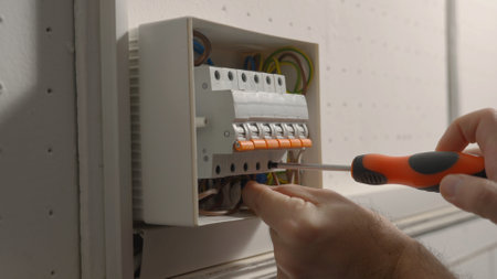 Electrician assembles electrical panel. Close up of a man hands tightening screw with a screwdriver in a switchboard high voltage electrical switches. Switch box with automatic fuses, wires, switches.の写真素材