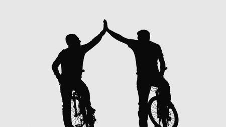 Back view on black silhouette of two cyclist greeting each other while sitting on bicycles on white background. The men strike with their hands, clapping their palms in gesture of greeting.の写真素材