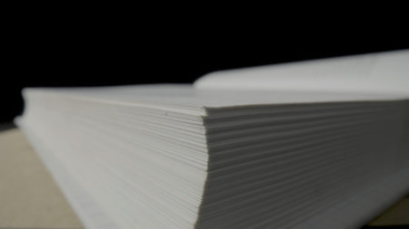 A stack of white pages of an open book that lies on a black isolated studio background. White empty sheets of paper book or textbook. Literary reading in the library, leisure. Macro shot of book pagesの写真素材