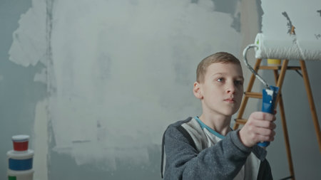 Teenager paints on glass with white paint using a roller. Young boy holds a roller in his hands and looks at the glass intently. Concept of repair, finishing works, interior design.の写真素材