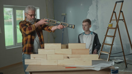 Grandpa shows his grandson how the water level installed on a brick wall works. An elderly man demonstrates the work of level and a teenager carefully looks and studies.の写真素材