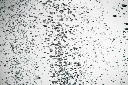 A lot of dark air bubbles of different sizes underwater on a white isolated background. Close up of light lit oxygen bubbles flow upwards. Aeration or filtration of liquid. Fizzy flow of air bubbles.の写真素材