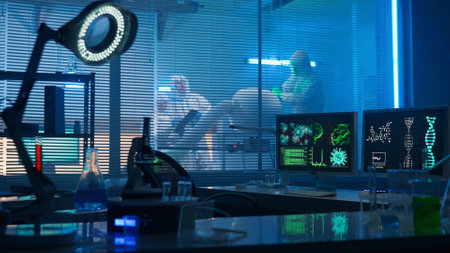 Modern medical research laboratory. Workplace of scientist or researcher with computers, microscope, test tubes, flasks and magnifying lamp. People in white hazmat suits are working in the background.の写真素材