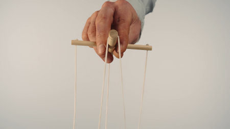 The puppeteers hand controls the puppet with a wooden manipulator and strings. The marionettist controls and pulls the strings on a white isolated background. Close up.の写真素材