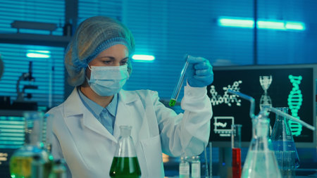 A female scientist is reviewing and researching a green liquid into a glass test tube. A woman in a...