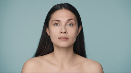 Close up portrait of a seminude woman on a blue background. A woman with natural make up looks straight ahead. Beauty concept. Natural beauty, cosmetology, skin care.の写真素材