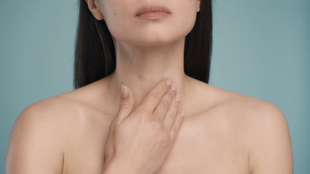 A woman applies cream to her neck. With slow massage movements, a woman rubs the cream into the skin close-up on a blue background. The concept of skin and body care. Natural beauty.の写真素材