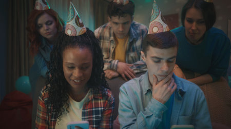 An African American girl and a Caucasian guy are playing an online game on their phones, friends...