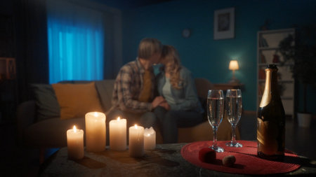 Glasses of champagne and a blurred loving couple in the background. A man and a woman in love are kissing while sitting on a sofa in the living room. Romantic candlelit evening with champagne, date.の写真素材