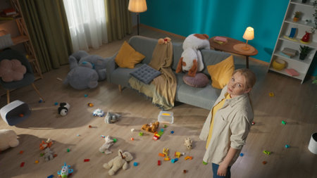 Mother standing and looking sad around the scattered toys in the living roomの写真素材
