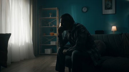 Dark silhouette of a man sitting in a room on a sofa in the dark, going through a crisis. A man...