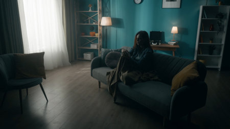 Devastated, detached, lonely young woman sits on a sofa in a dark room. Woman desperately thinking about personal problems, going through a crisis. Hopelessness. The concept of mental health.の写真素材